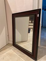 Full view of framed mirror showing rectangular shape, wooden frame with brown and red tones, and the reflective glass surface.