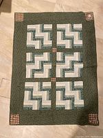 Full view of the green handmade quilt laid flat on the floor, showing overall pattern and size.
