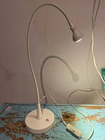 Full view of the white IKEA table lamp showing flexible gooseneck, circular base, and inline switch on cord
