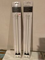 Two white magnetic cafe curtain rods in original packaging, standing upright