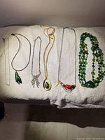 Full view of all seven necklaces laid out on a white towel, showing variety of styles including beaded, cord, and chain types with assorted pendants.