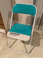 Front view of the folding chair showing turquoise seat and backrest with the Pantone 15-5519 label.