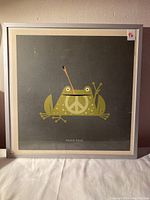 Framed print featuring a green frog with a peace symbol and peace sign gesture.