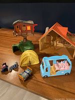 Photo showing multiple Playmobil structures and toys arranged on a wooden surface including a treehouse, house, tent, toy bus and cradle.