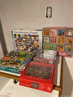 Wide view of puzzle boxes showing multiple boxed puzzles including Ravensburger, Springbok, and other brands, stacked on a table