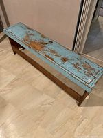 Front and side view of rustic wooden bench showing distressed light blue paint on seat and natural wood base and legs.