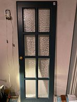 Full view of the teal kitchen cupboard door showing all glass panels and gold knob