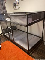 View of the gray metal twin bunkbed frame showing the ladder and safety mesh on side rails.