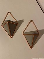 Two Umbra wall hangers mounted on light-colored surface, showing gray ceramic vessels in copper triangular frames.