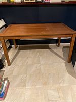 Full view of the rectangular wood dining table sitting on tiled floor against dark wall background.