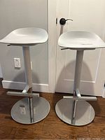Front view of two white adjustable bar height stools with round chrome bases and footrests.