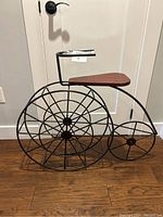 Front view of bicycle-shaped wine holder showing large wheel design and wooden seat.