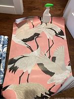 Pink and white crane wallpaper laid out flat on wood floor with a spray bottle on top for scale.