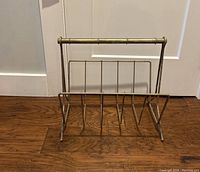 Front angle view of the vintage metal magazine holder on wooden floor showing bamboo style handle and angled slots for separating magazines.