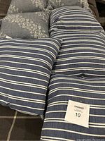 Four blue and white striped outdoor pillows stacked and tagged with lot number 10.