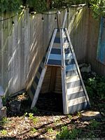 Front view of wooden teepee with blue and white painted stripes. Opening visible at front.