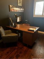 Side angle view of main desk piece against dark wall with window, showing desk surface and storage drawers below, upholstered chair beside desk.