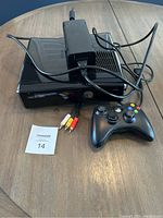 Xbox 360 console with power supply, controller, and composite AV cable on round wooden table.