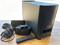 Front view showing subwoofer, two satellite speakers, remote control, power module and cables arranged on table