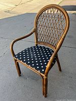 Front view of a cane arm chair with a curved topback and lattice design on the backrest. The seat has a black fabric cushion with white polka dot pattern.