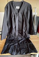 Front view of black graduation robe hung on hanger on table.