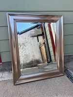 Silver-framed mirror with wide metallic frame leaning against exterior wall