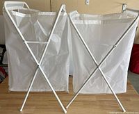Two white foldable laundry baskets with plastic bags and white metal frames, shown side by side