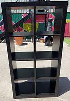 Front view of dark brown Ikea Kallax shelf unit showing the 8 cubby compartments in 2 rows and 4 columns, outdoors in sunlight.