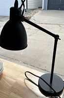 Close-up side view of black metal desk lamp showing adjustable arm, conical shade, round base, and cord.