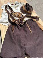 Photo showing men's dark brown lederhosen shorts with embroidered suspenders and white shirt, laid flat on surface