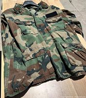 Camouflage jacket displayed on a hanger showing front with pockets and button details