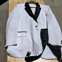 White tuxedo jacket with black satin lapels, black trim on pockets, and black cummerbund on wooden table outdoors.