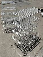 Photo showing multiple white mesh stackable shelves of various sizes in a group on concrete surface