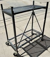 Full view of black metal rolling folding table with perforated two-section top and support braces on caster wheels