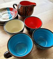 Close view of mugs, bowls, creamer pitcher, and plates on wooden table showing colors and patterns