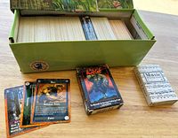 Photo showing approximately 500 cards in a long green collector's box with loose cards and two card boxes on top. Visible cards are Rage trading cards with dark fantasy illustrations. Includes one smaller Music Playing Cards deck box.