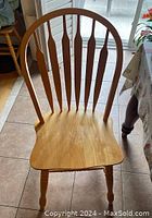 Front view of a single wooden dining chair showing curved spindle back, contoured seat, and turned legs