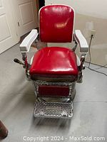 Front view of vintage barber chair showing red vinyl upholstery, chrome frame, white armrests, and metal footrest