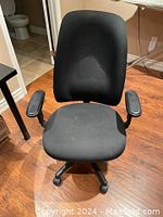 Single black office chair showing padded fabric seat, backrest, and armrests with five-wheel base on wooden floor.
