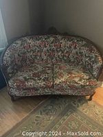 Front view of French Provincial loveseat with floral upholstery and carved wood frame.