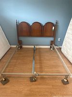 Full view of the bed frame including the headboard attached to metal bed frame with caster wheels, placed on a wooden floor next to mattresses.