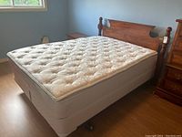 Bed with wood veneer headboard, mattress, box spring and metal frame on wooden floor near window