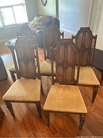 Set of six wood veneer dining chairs with cane backs and light tan upholstered seats placed on wooden floor in living room area.