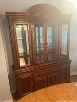 Front view of two-piece wood veneer china cabinet showing buffet with 1 center drawer and 4 cabinets, hutch with 4 glass inset doors, side panels and arched top.