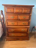 Front-right angled photo of wood veneer dresser showing five drawers with metal pulls and scalloped base.