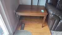 Full top and lower shelf view of brown wood end table with scratches by a sliding glass door and sofa.