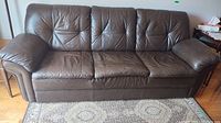Front view of the brown leather three-seat sofa showing worn cushions and leather texture.