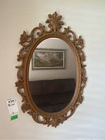 Full view of oval wall mirror with ornate composite frame against white wall showing decorative floral and scroll elements.