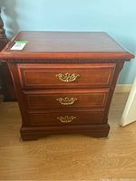 Front view of wood veneer night stand showing three drawers and metal decorative pulls.