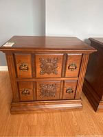 Front view of wood veneer night table showing two drawers, carved decorative panels, and metal ring pull handles.